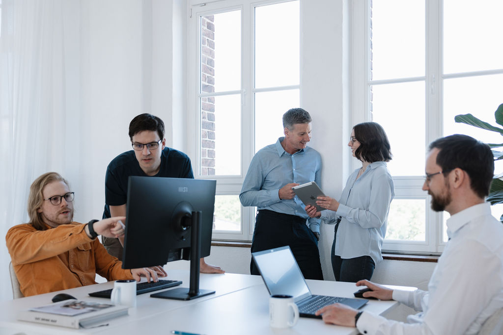 Team arbeitet gemeinsam an Computern und bespricht digitale Prozesse.
